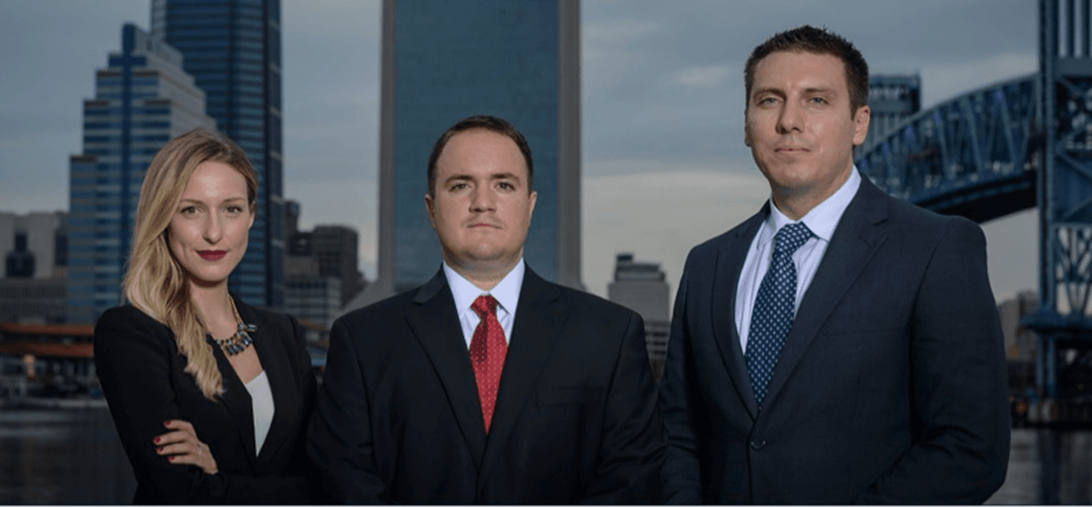 Three professionals standing together outdoors in a city, dressed in business attire, with skyscrapers and a bridge in the background.